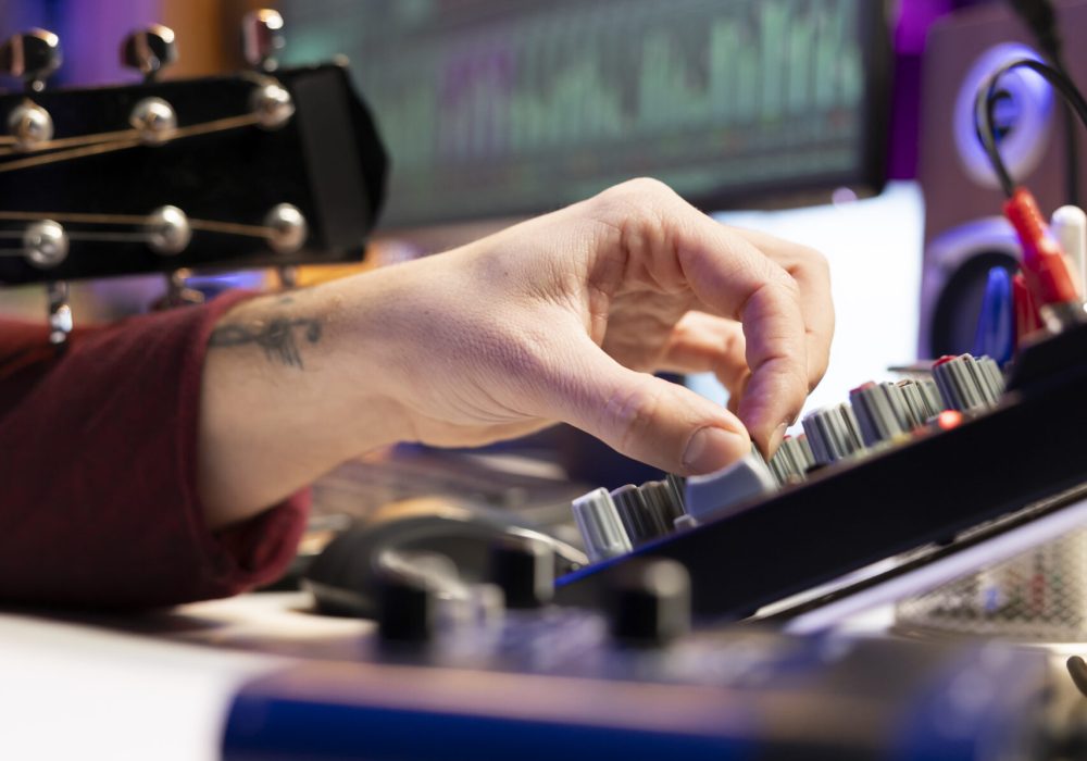 Music producer twisting pre amp knobs on mixing console to edit audio recordings in home studio, works with stereo equipment to create tunes. Artist plays guitar, acoustical engineering. Close up.